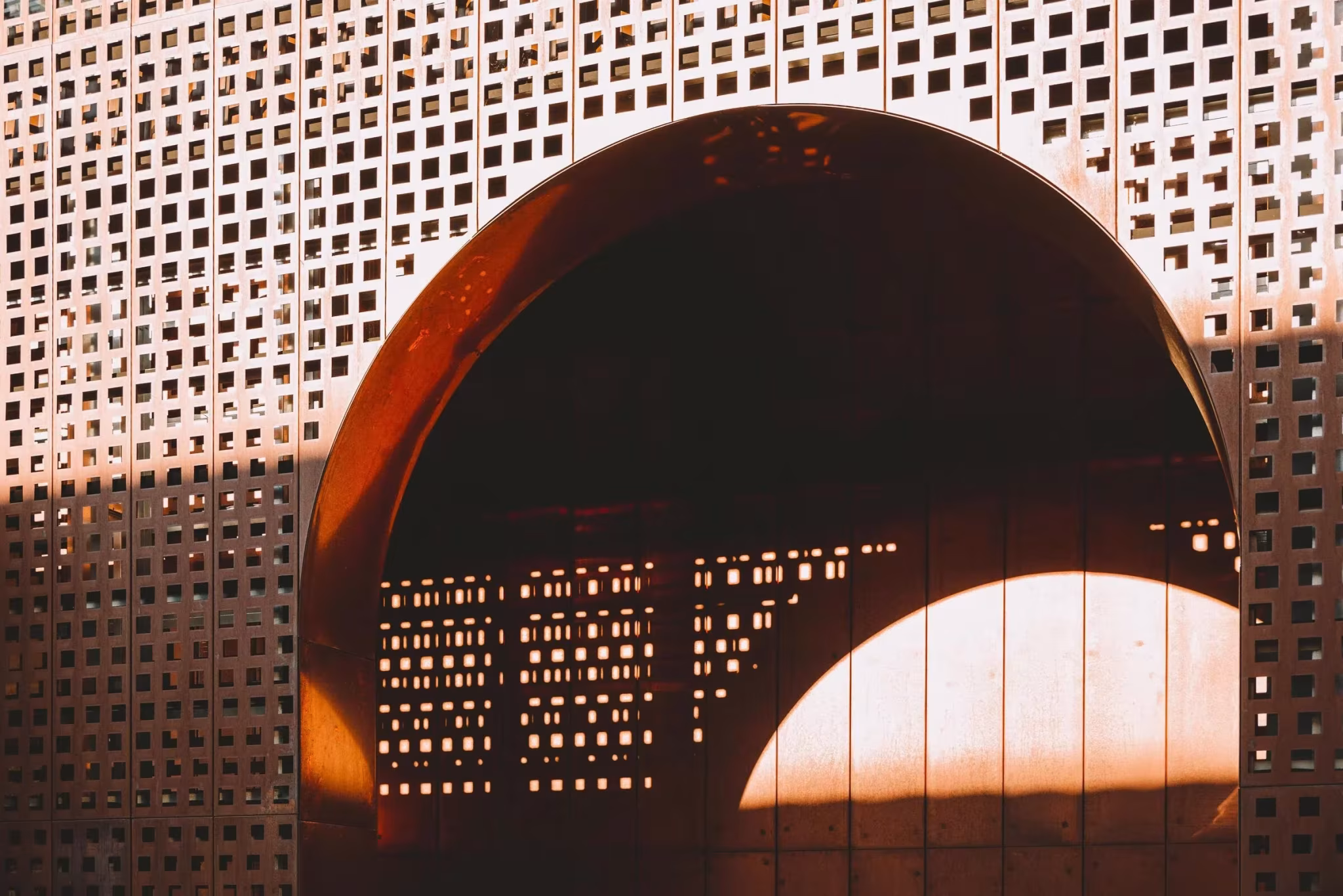 Arco de corten visto desde el interior a través de la celosía perforada con luz de atardecer en el Convento Saint-François