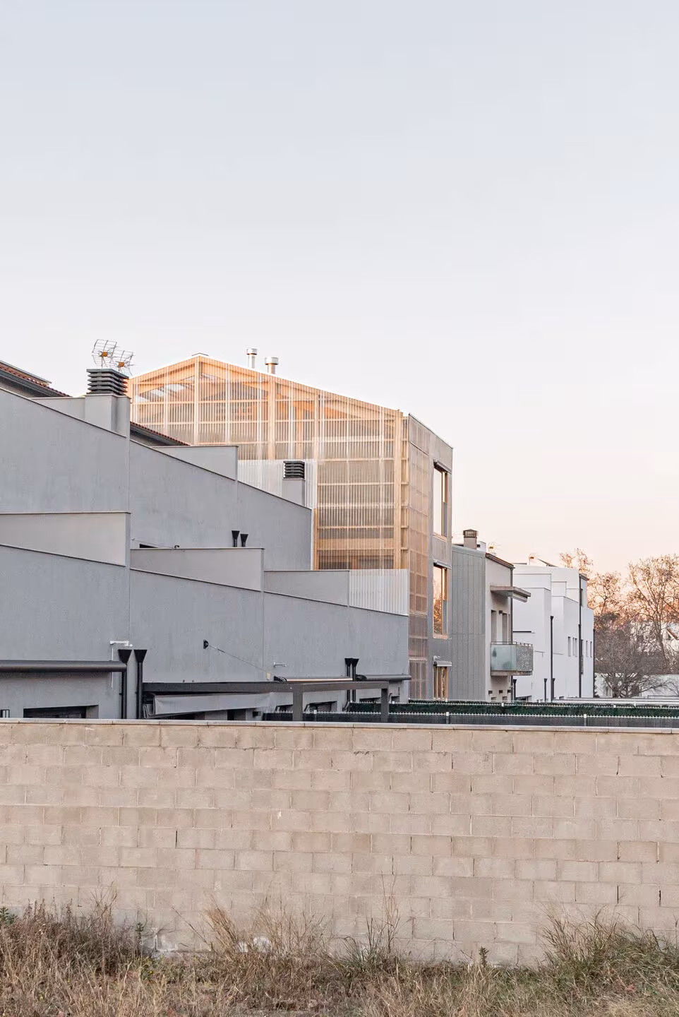 Casa0006 de Taller11 con el volumen de cubierta acristalada de madera tras las viviendas vecinas al atardecer