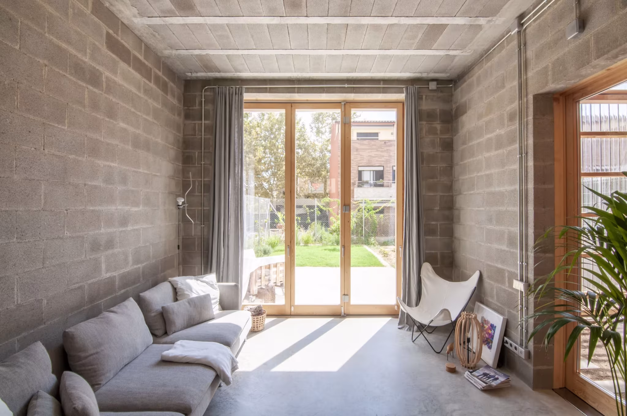 Salón de la Casa0006 con muros de bloque de hormigón, sofá gris y puerta acristalada al jardín