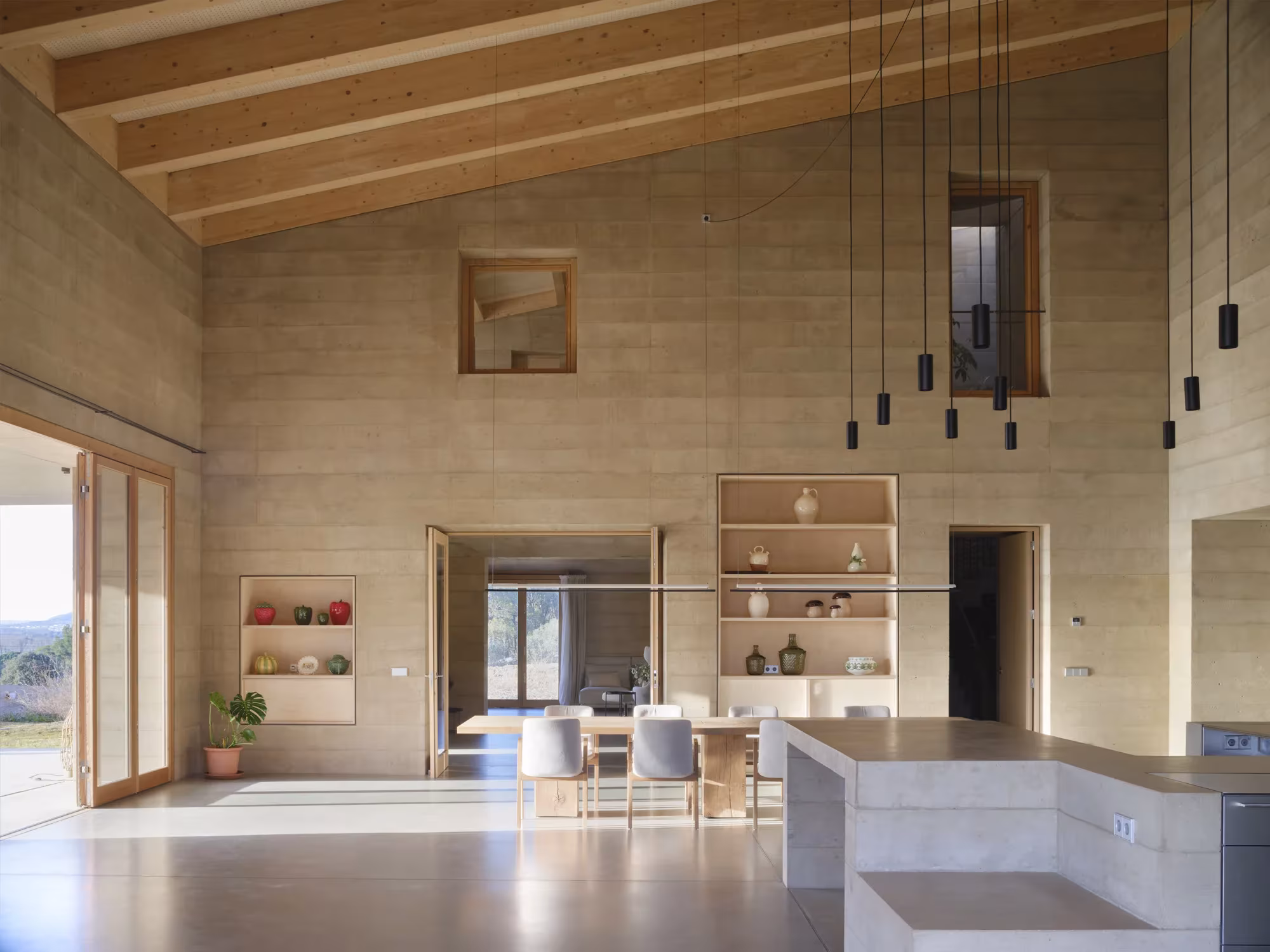 Cocina y comedor de la Casa 1627 bajo un techo de madera, con lámparas colgantes y muros de tierra