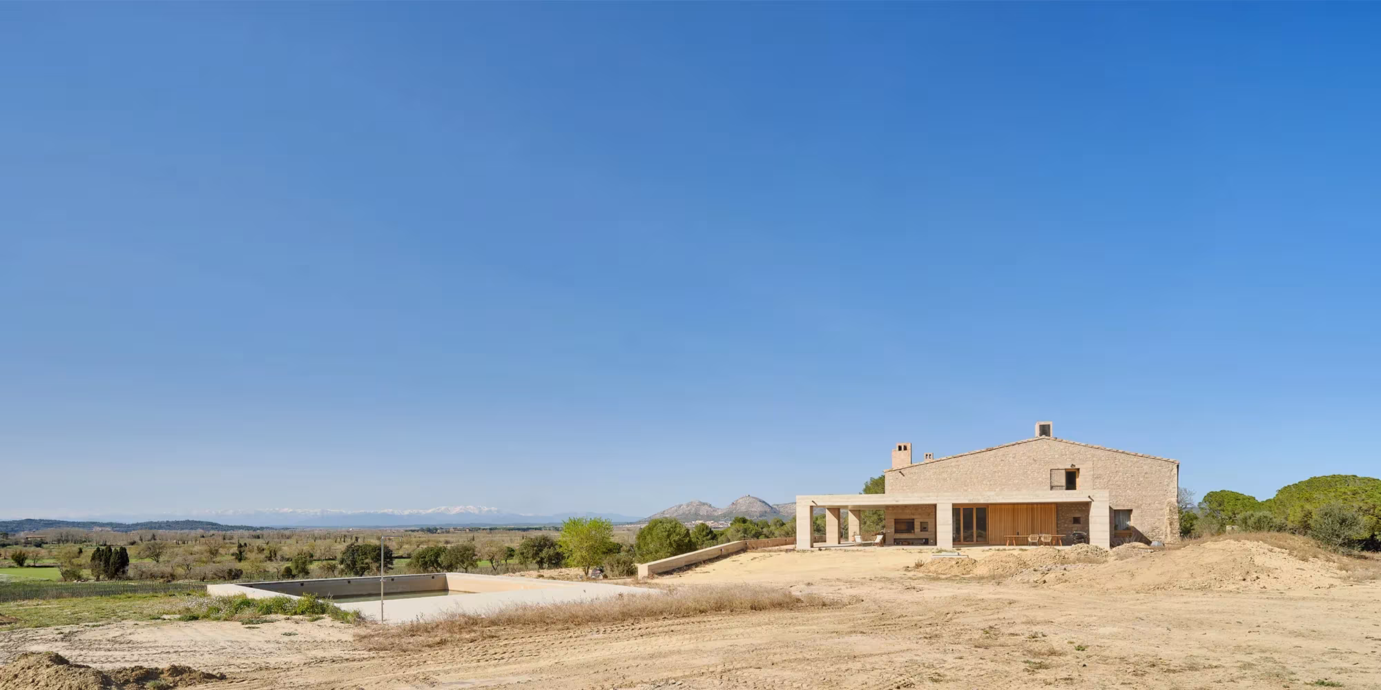 Casa 1627 en el paisaje abierto, un conjunto bajo de piedra visto a distancia bajo un cielo despejado