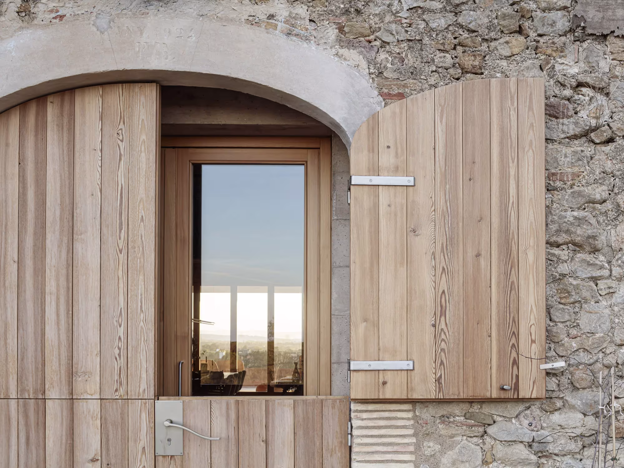 Ventana en arco con contraventanas de madera abiertas sobre el muro de piedra de la Casa 1627
