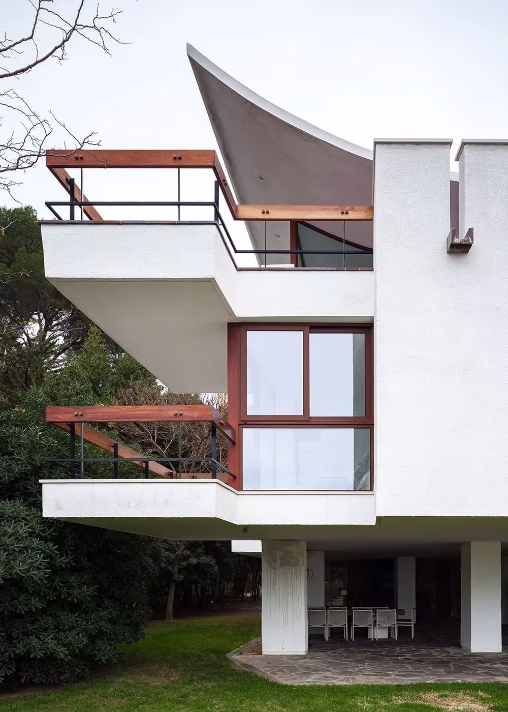 Terrazas voladas con carpintería de madera rojiza y marquesina curva blanca en la Casa Cruïlles