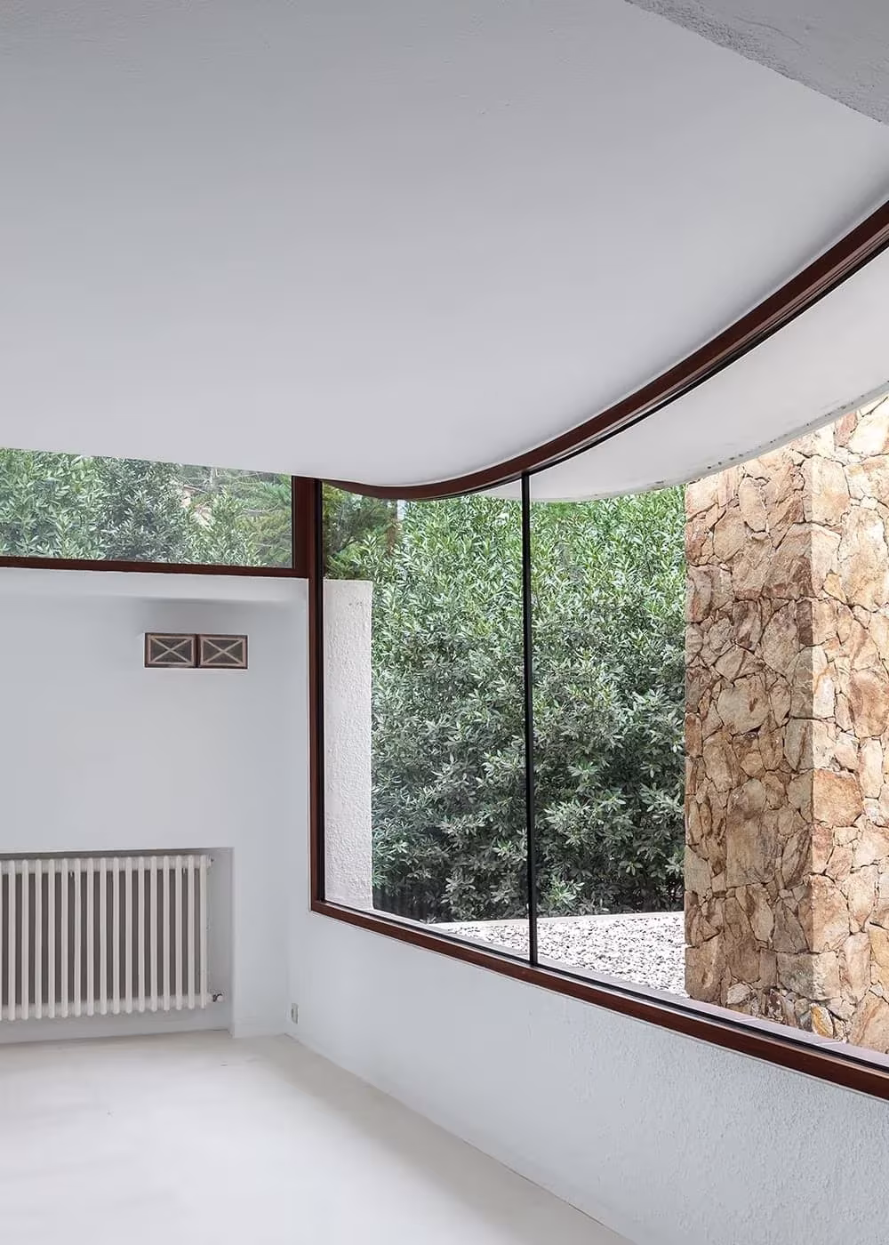 Ventana de esquina curva con marco de madera oscura frente a un muro de piedra en la Casa Cruïlles