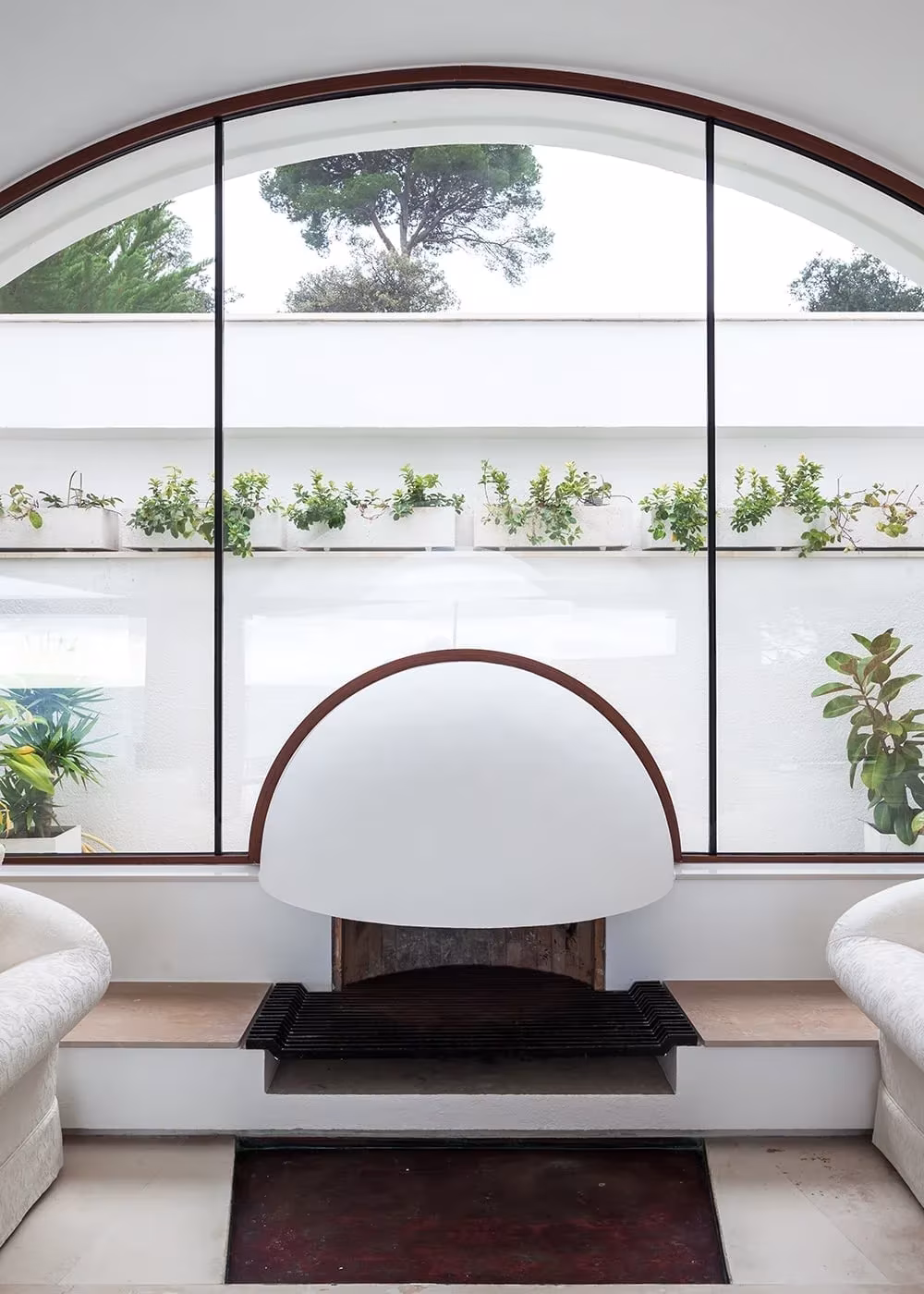 Chimenea blanca de campana bajo un ventanal en arco con jardineras en el salón de la Casa Cruïlles
