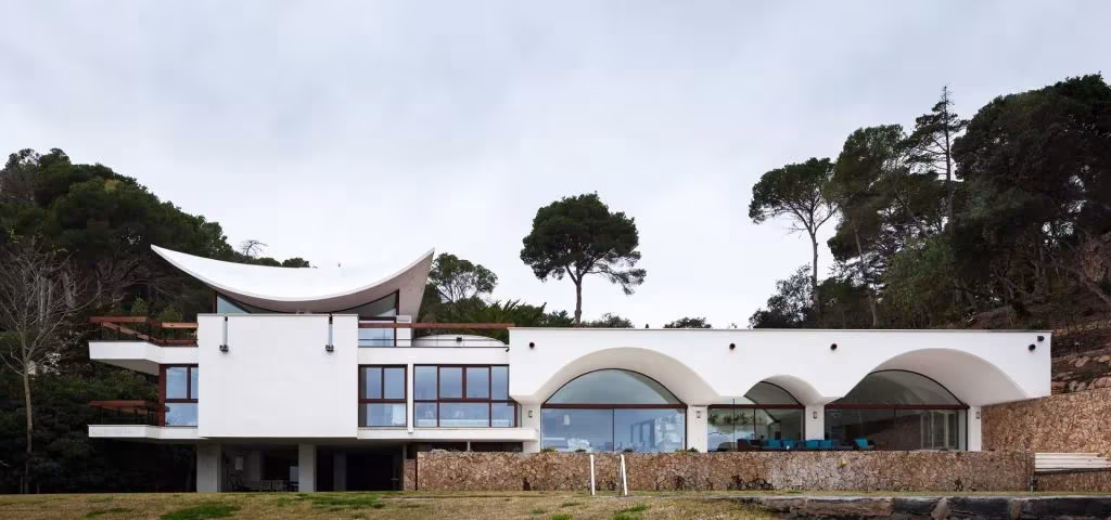 Casa Cruïlles de 1968 con cubierta alabeada blanca y arcos de bóveda en el frente acristalado entre pinos