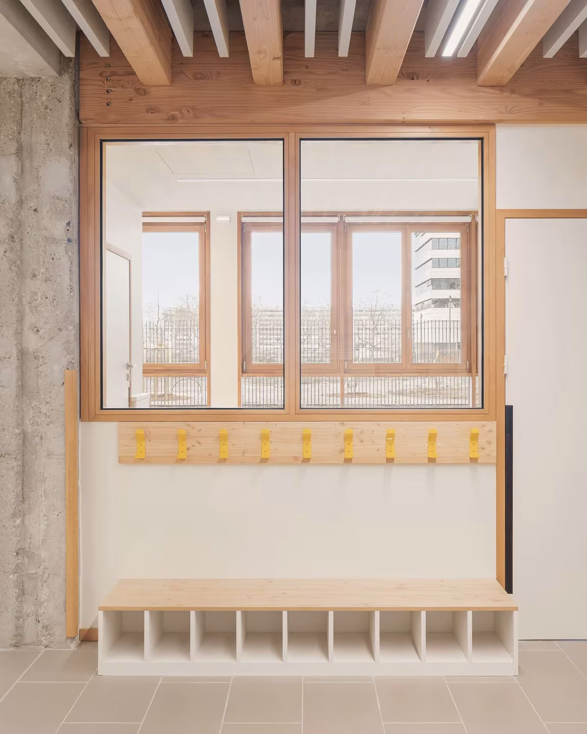 Rincón de entrada con casilleros, perchas amarillas y ventana de madera en la escuela del mercado de Lyon