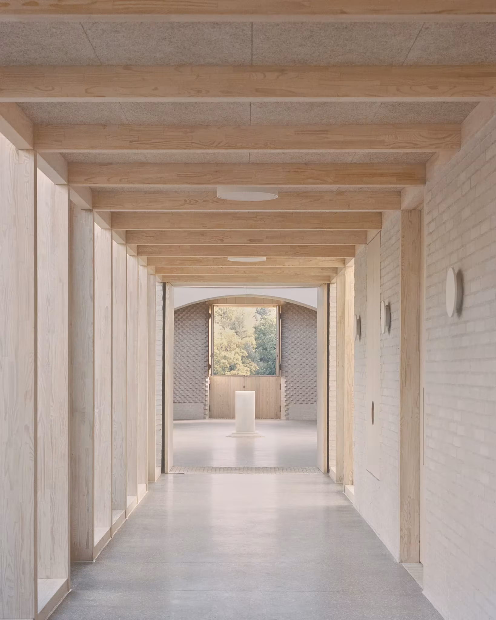 Pasillo con techo de vigas de madera y paredes de ladrillo claro hacia la sala central del New Temple Complex
