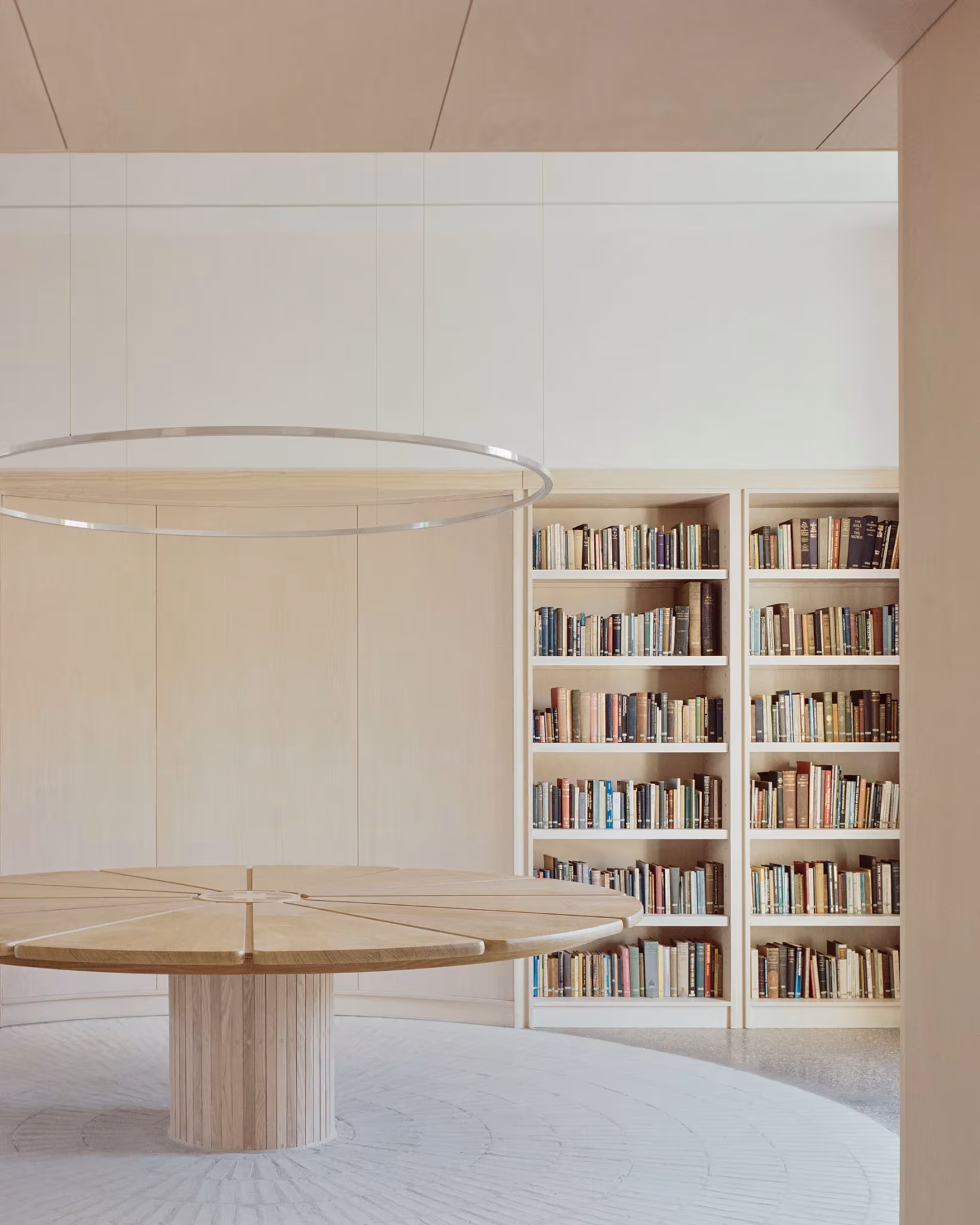 Mesa redonda de madera ante una librería y bajo un anillo luminoso en el New Temple Complex