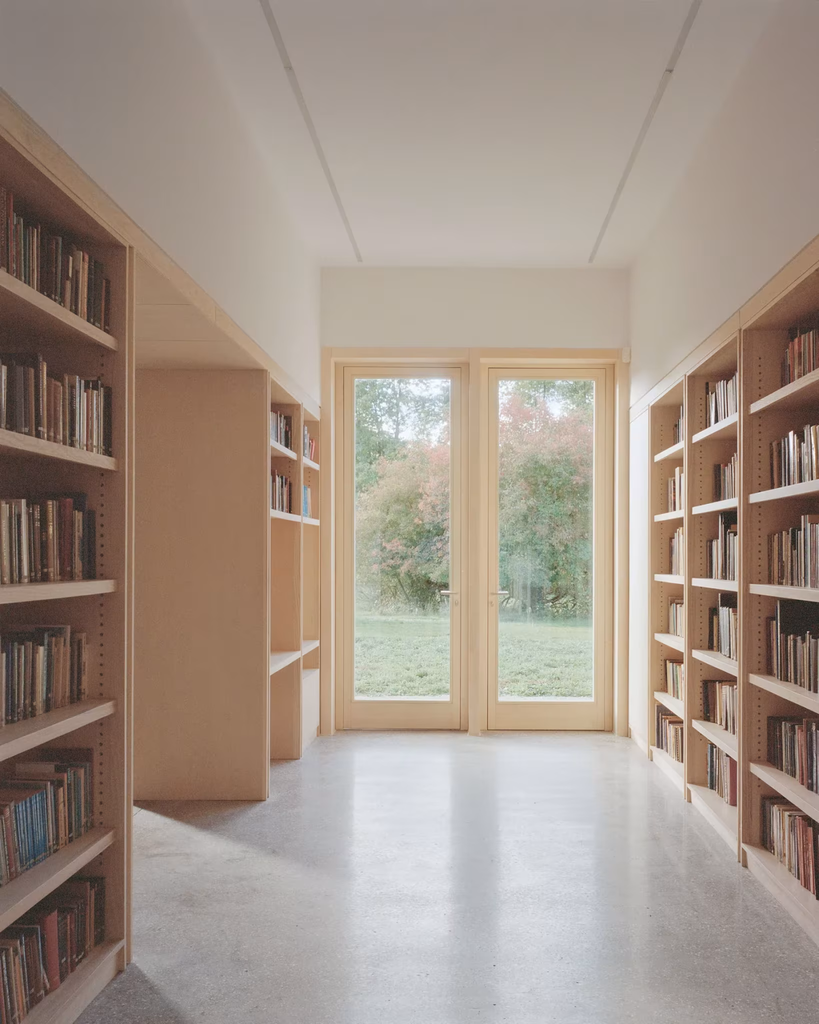 Sala de lectura con estanterías de madera llenas de libros y puerta acristalada al jardín en el New Temple Complex