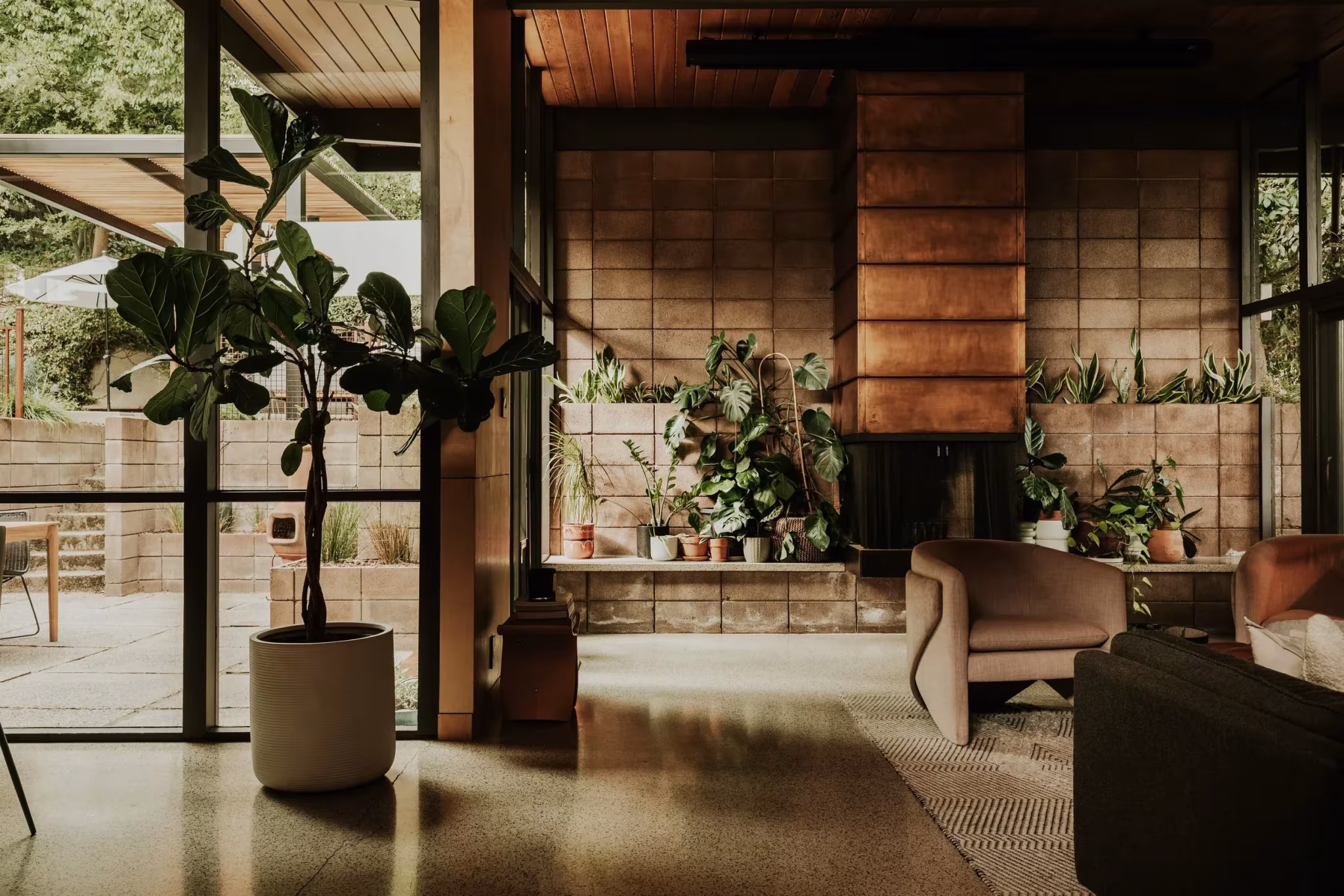 Salón de la Residencia Nittler con ficus, chimenea de bloque y terraza vista a través de la cristalera