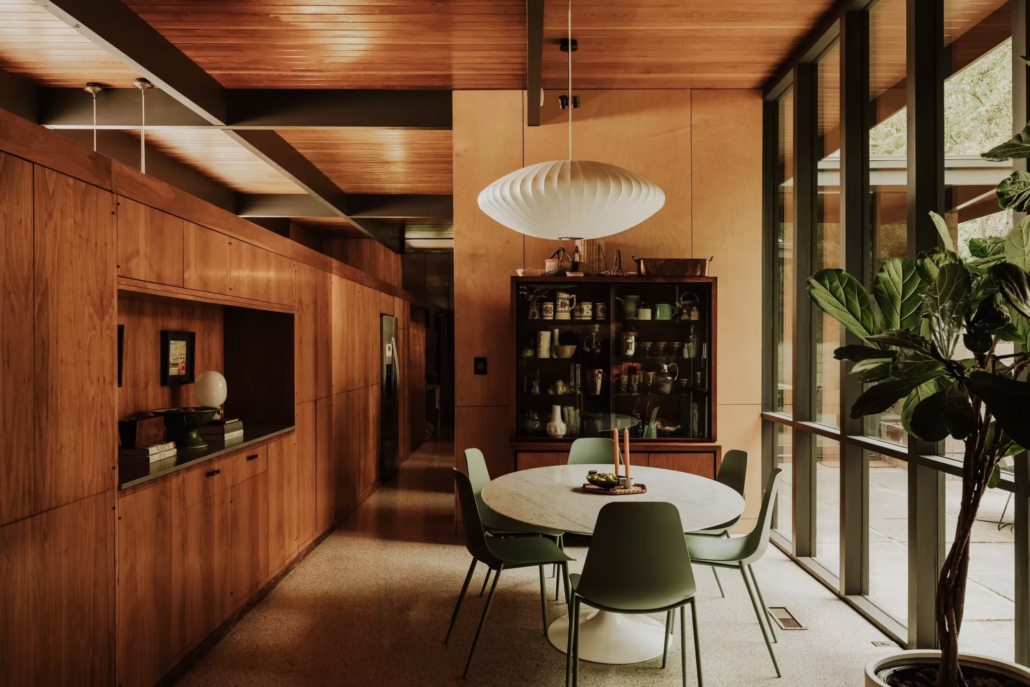 Eje de la Residencia Nittler con comedor de mesa redonda, armarios de madera y cristalera hacia el jardín