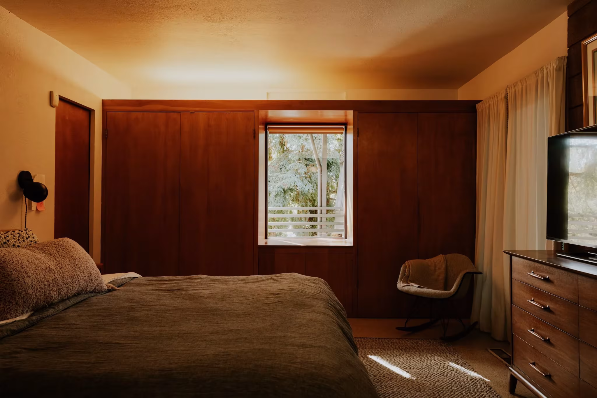 Dormitorio principal de la Residencia Nittler con paredes de madera y ventana sobre un cabecero bajo