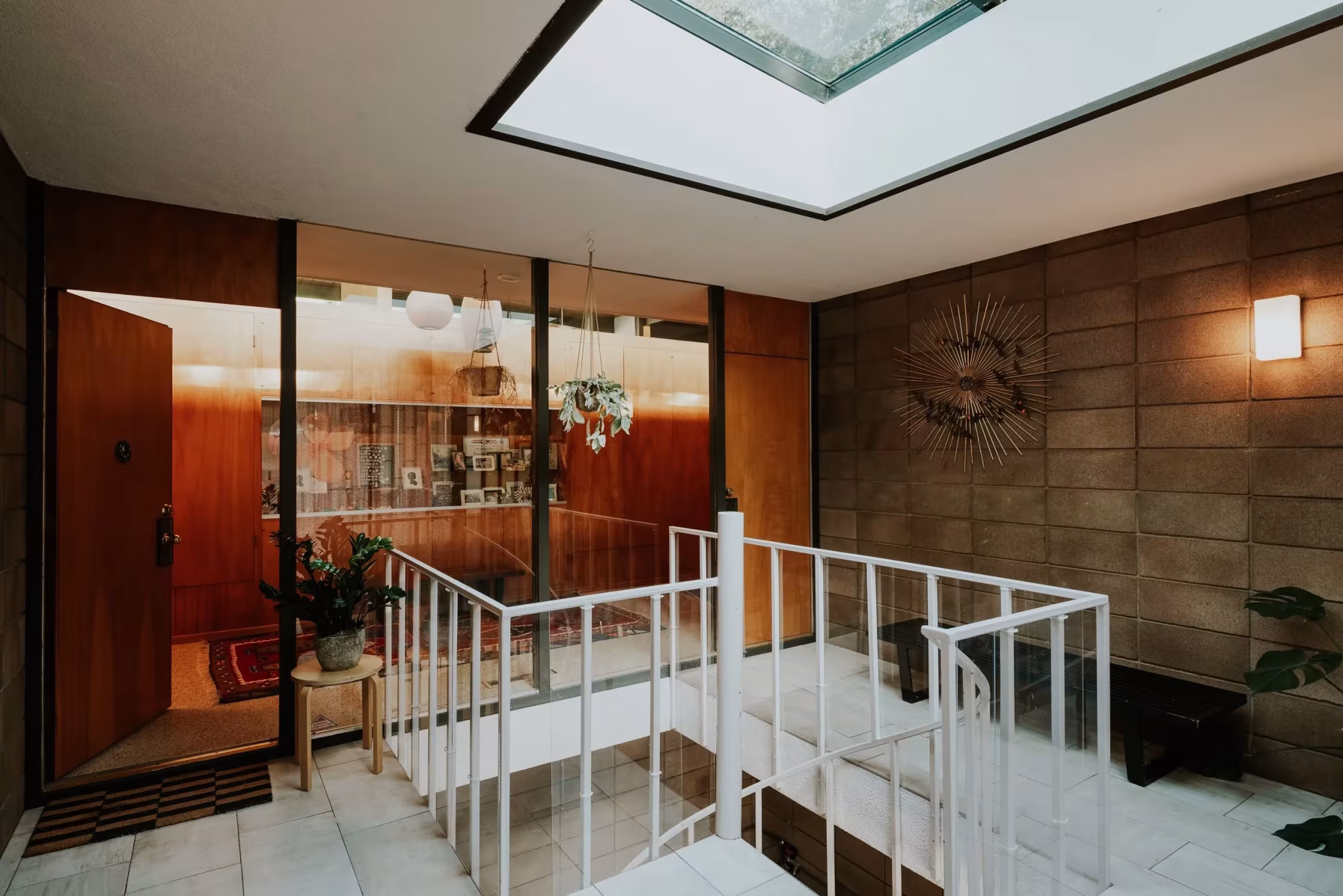 Entrada de la Residencia Nittler con tragaluz, barandilla blanca y muros de bloque ante un panel de madera