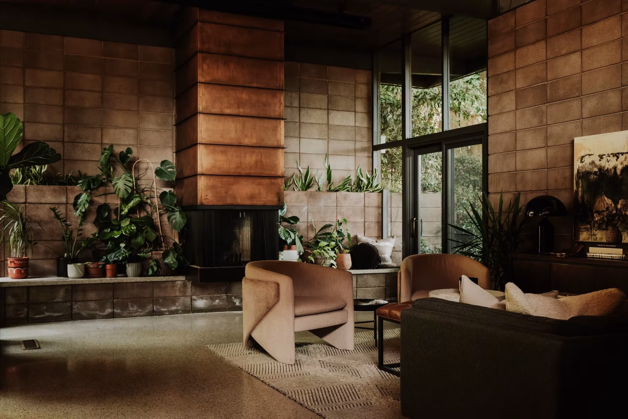 Salón de la Residencia Nittler con chimenea de bloque de hormigón, plantas y ventanales de suelo a techo