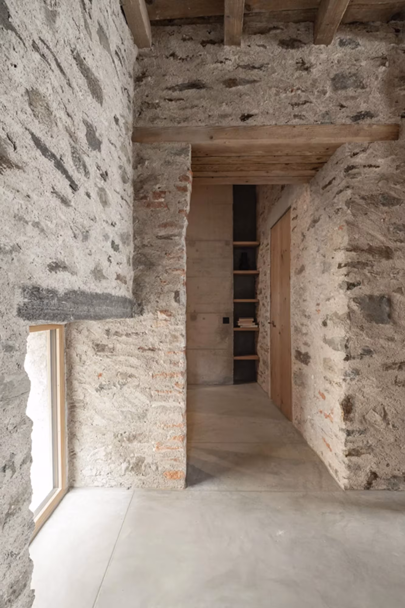 Quiebro de muro de piedra con carpintería de madera y estantería empotrada en Transformation House ME