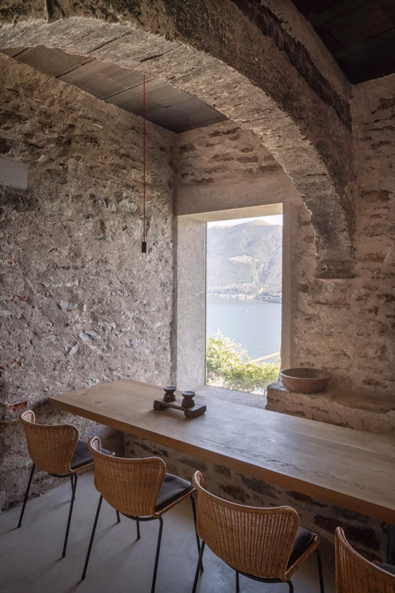 Mesa de madera junto a una ventana sobre el lago bajo un arco de piedra en Transformation House ME