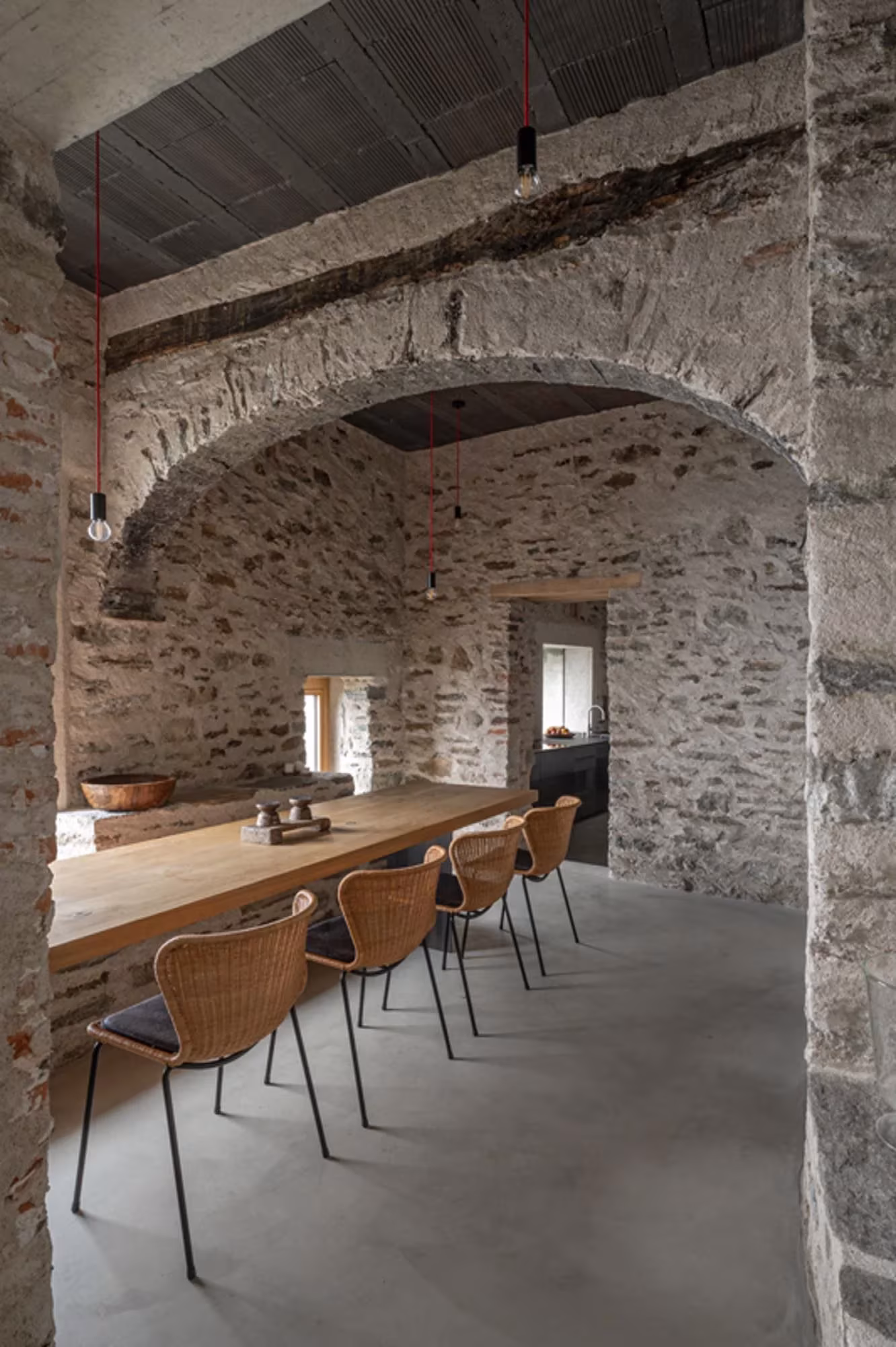 Comedor bajo un arco de piedra con mesa larga de madera y sillas de mimbre en Transformation House ME
