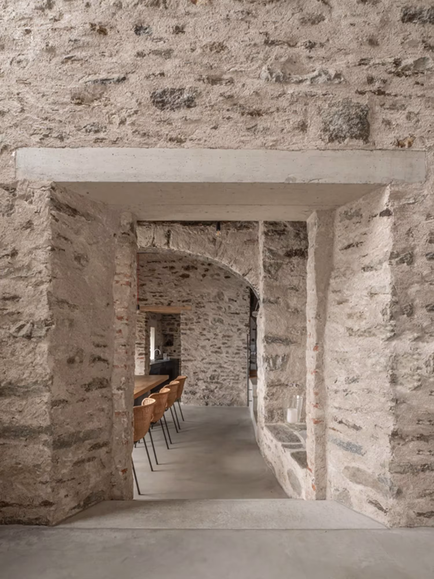 Paso en el muro de piedra con dintel de hormigón hacia el comedor en Transformation House ME