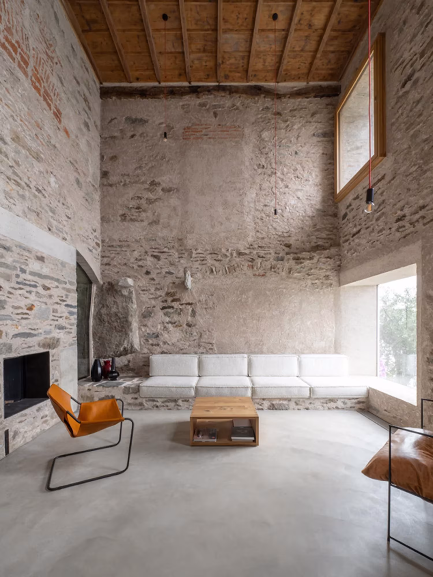 Sala de doble altura con muros de piedra, sofá blanco corrido y techo de madera en Transformation House ME