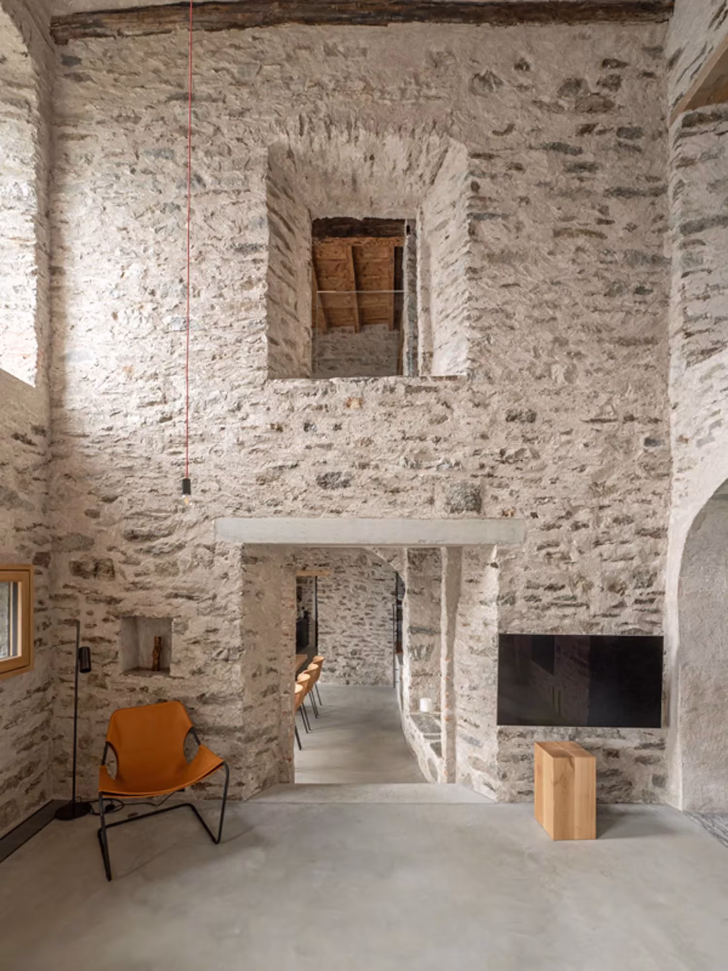 Salón de muros de piedra vista con hueco alto, sillón de cuero y paso a otra sala en Transformation House ME