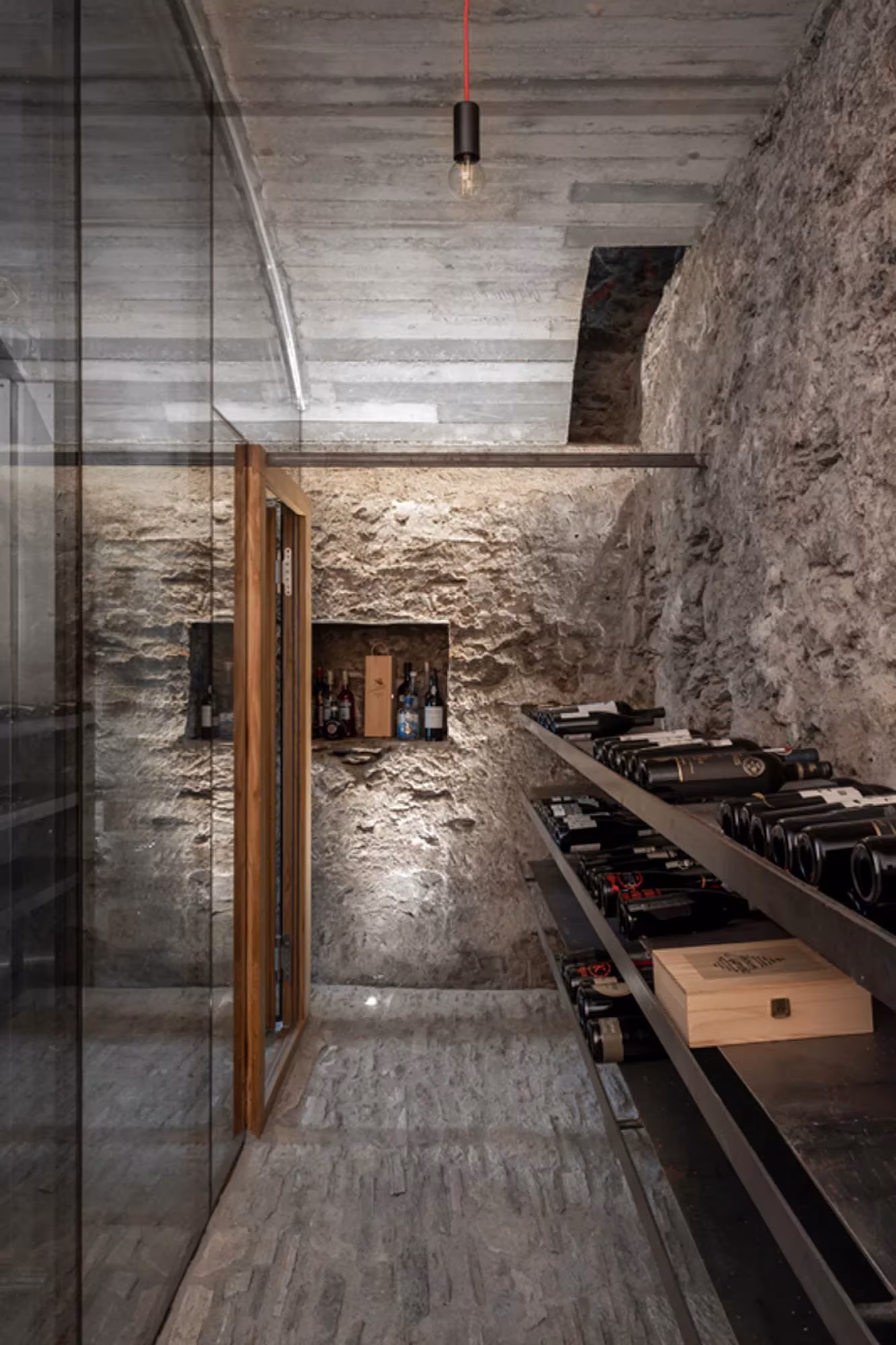 Cocina con barra de acero oscuro tras un cerramiento de vidrio y muro de piedra en Transformation House ME