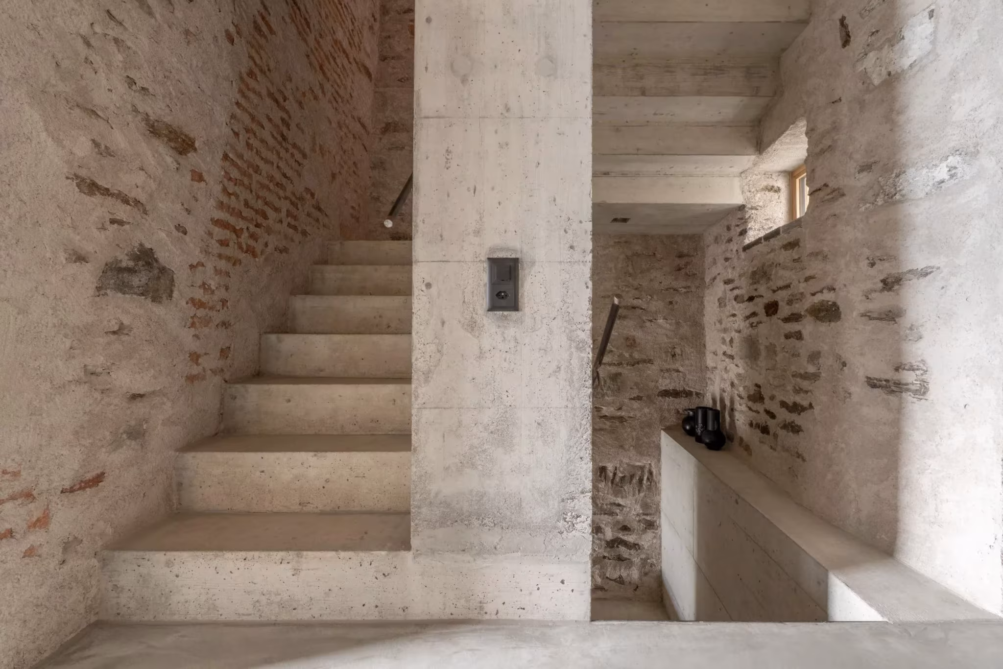 Escalera de hormigón visto junto a muros de piedra y ladrillo en Transformation House ME