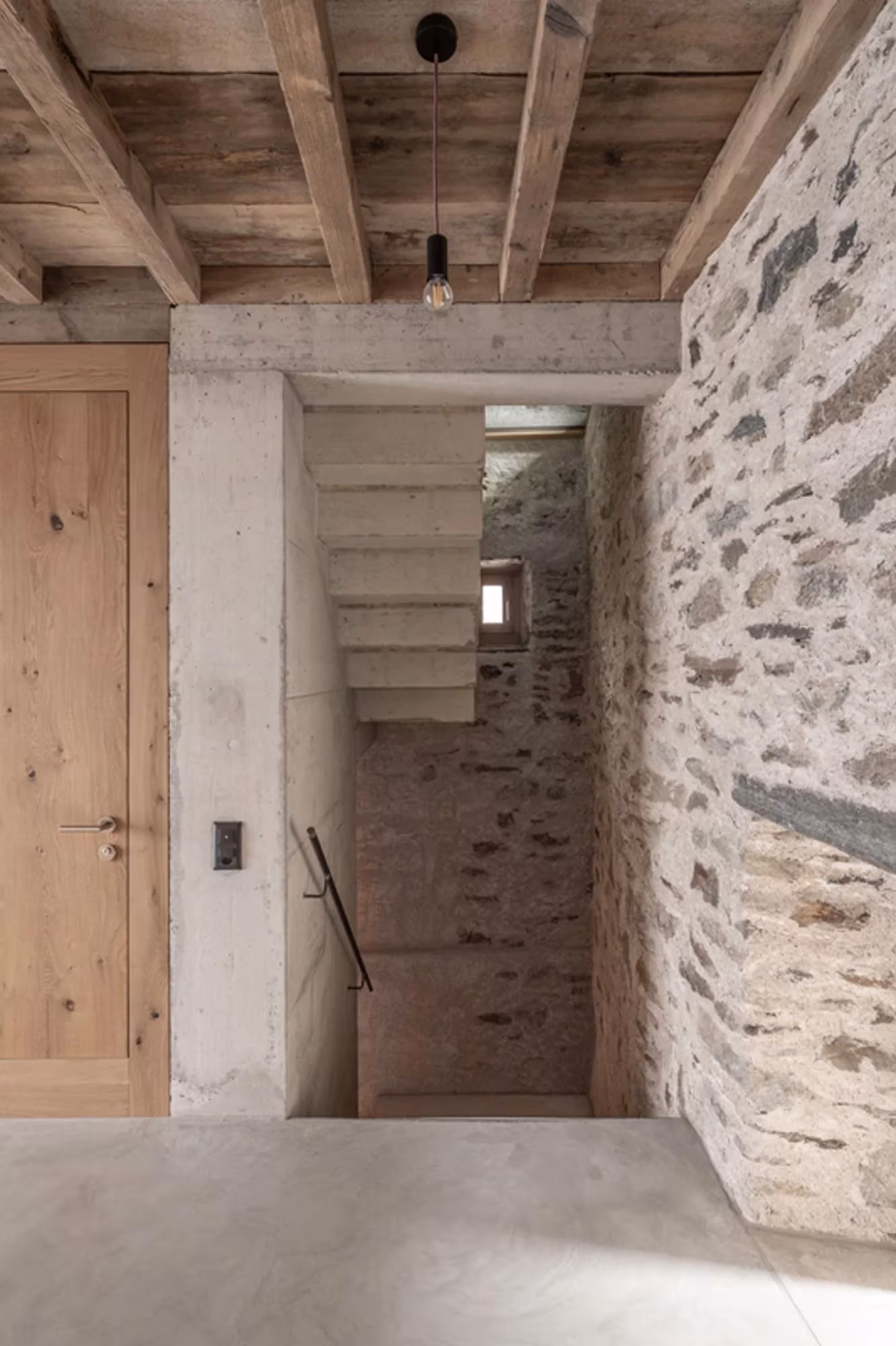 Escalera de hormigón con puerta de roble y forjado de vigas entre muros de piedra en Transformation House ME
