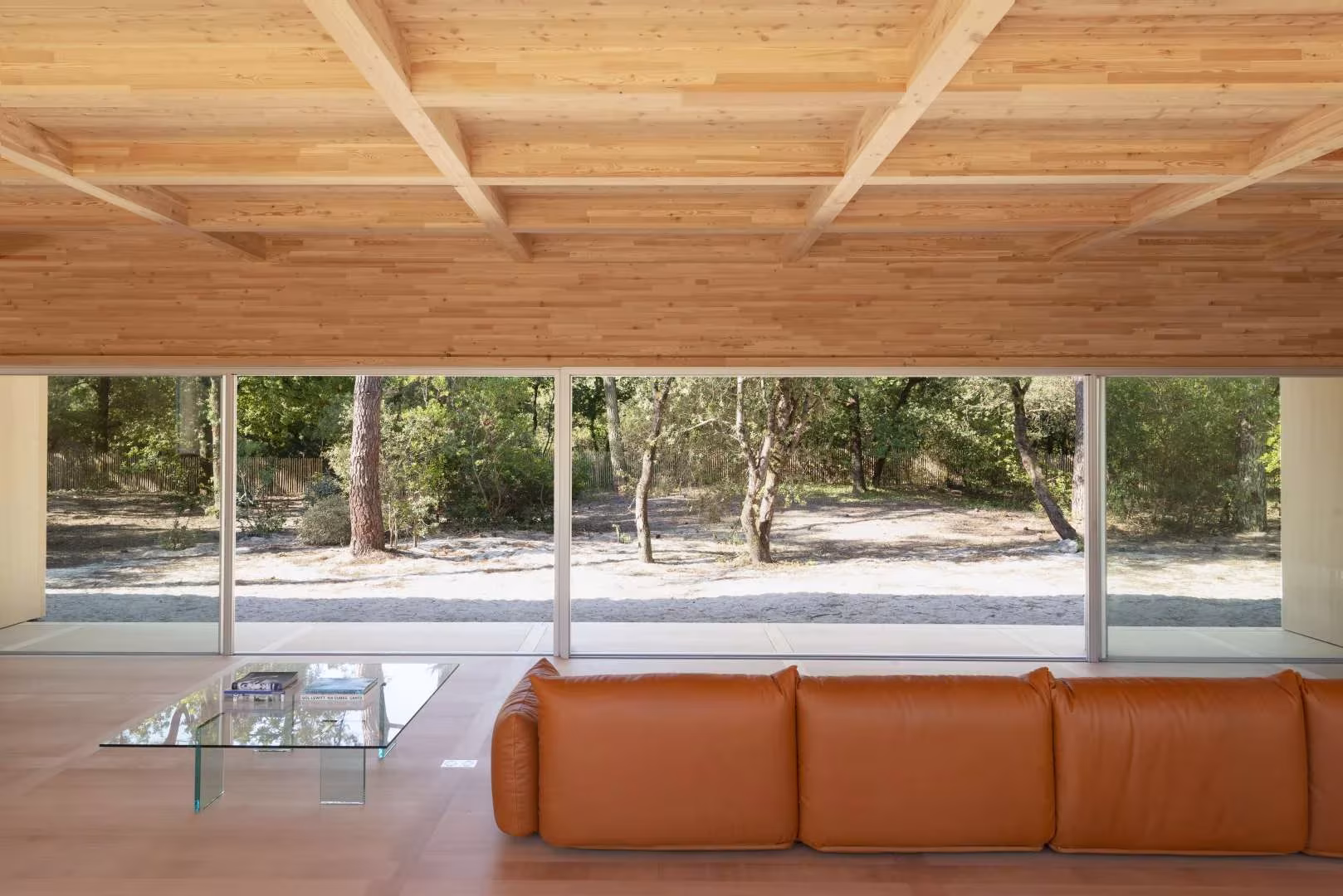 Sala de la Maison en Bois con sofá de cuero, techo de casetones de madera y cristalera al bosque