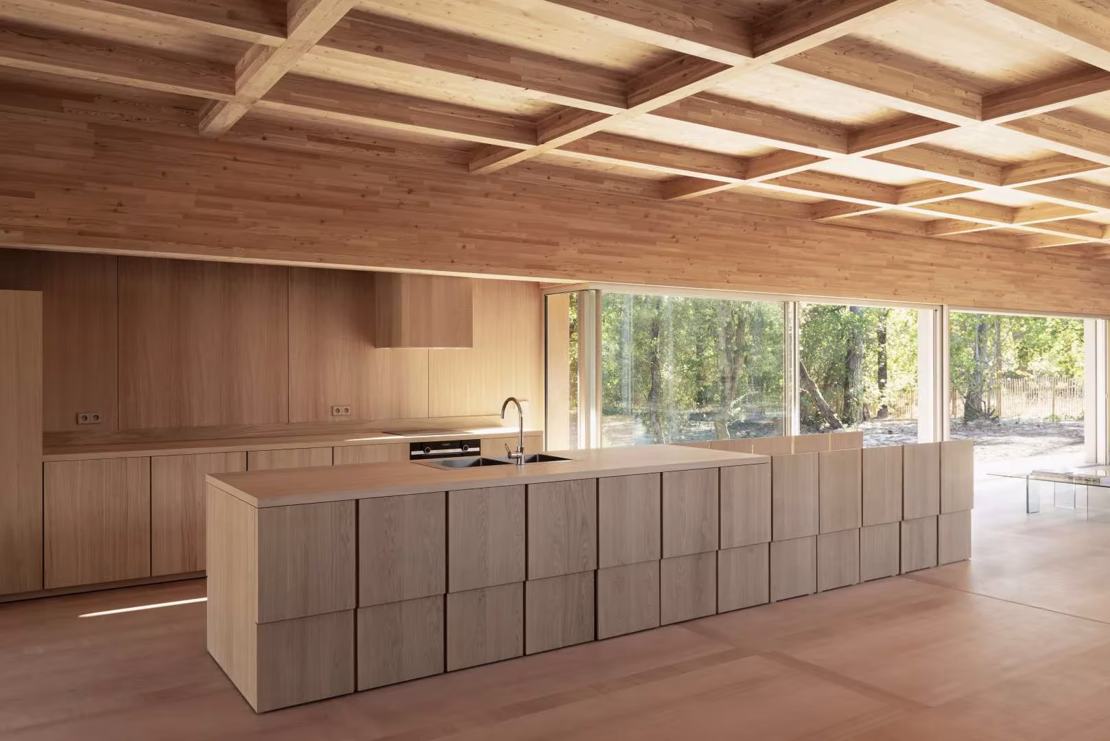Isla de cocina modular de madera frente a la cristalera del bosque en la Maison en Bois