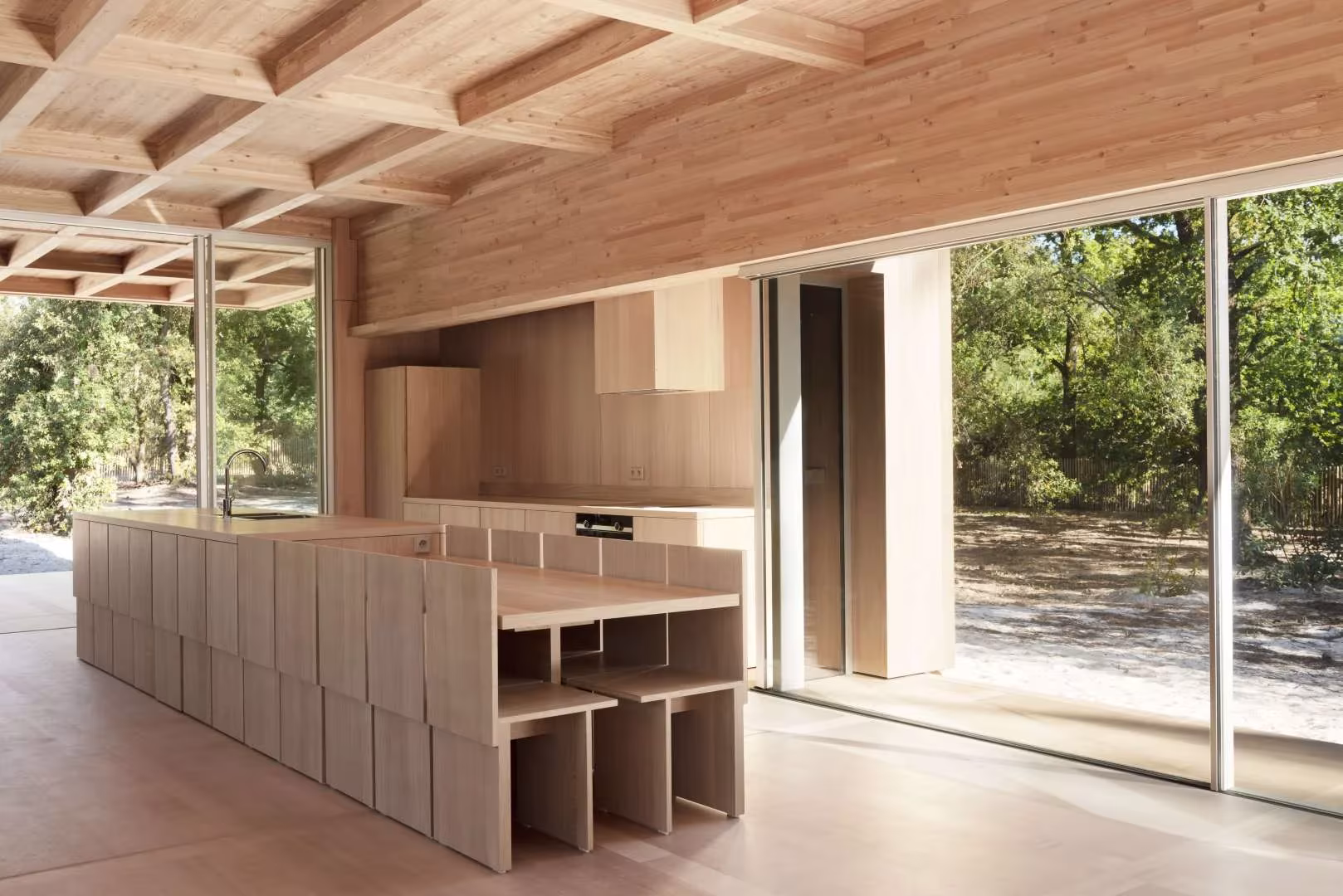 Mueble bajo de módulos de madera que separa estancias en la Maison en Bois entre cristaleras al bosque