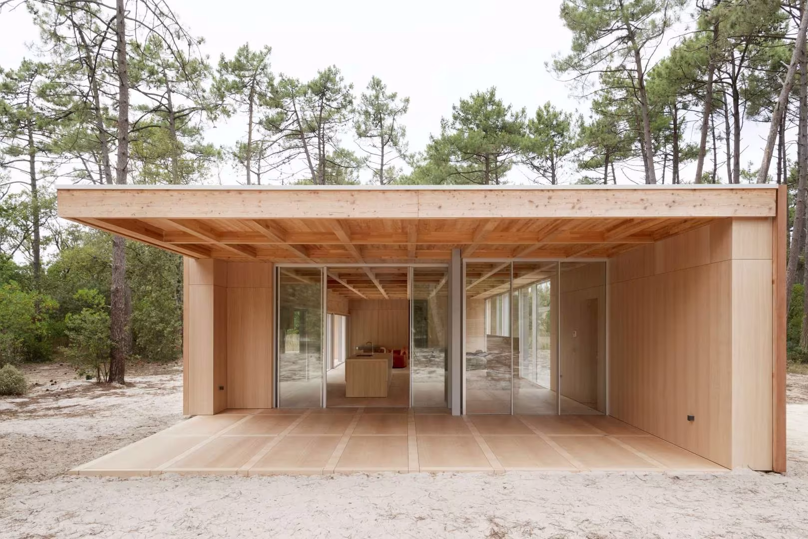 Porche de la Maison en Bois con cubierta de madera y fachada de vidrio que se abre al pinar