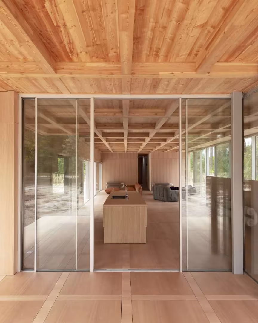 Cerramiento de vidrio corredero que deja ver la isla de madera de la Maison en Bois desde el pinar