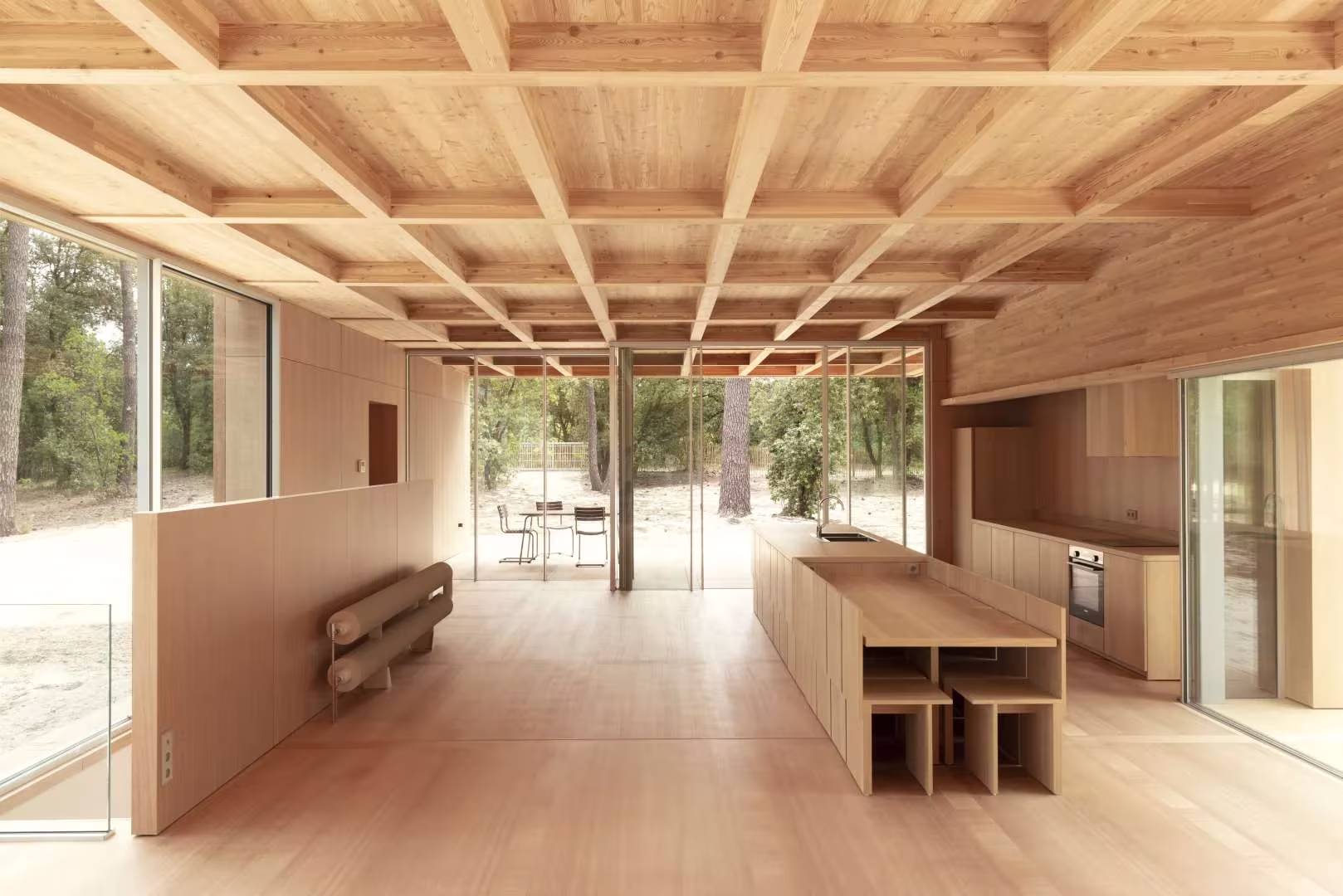 Cocina con isla de madera y mueble divisorio bajo el artesonado de la Maison en Bois