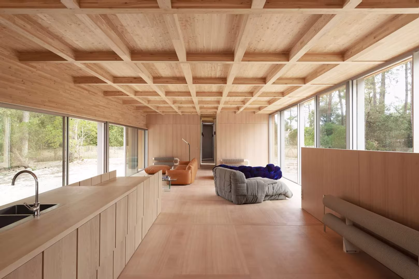 Cocina corrida con frentes de madera y sala bajo el techo de casetones de la Maison en Bois
