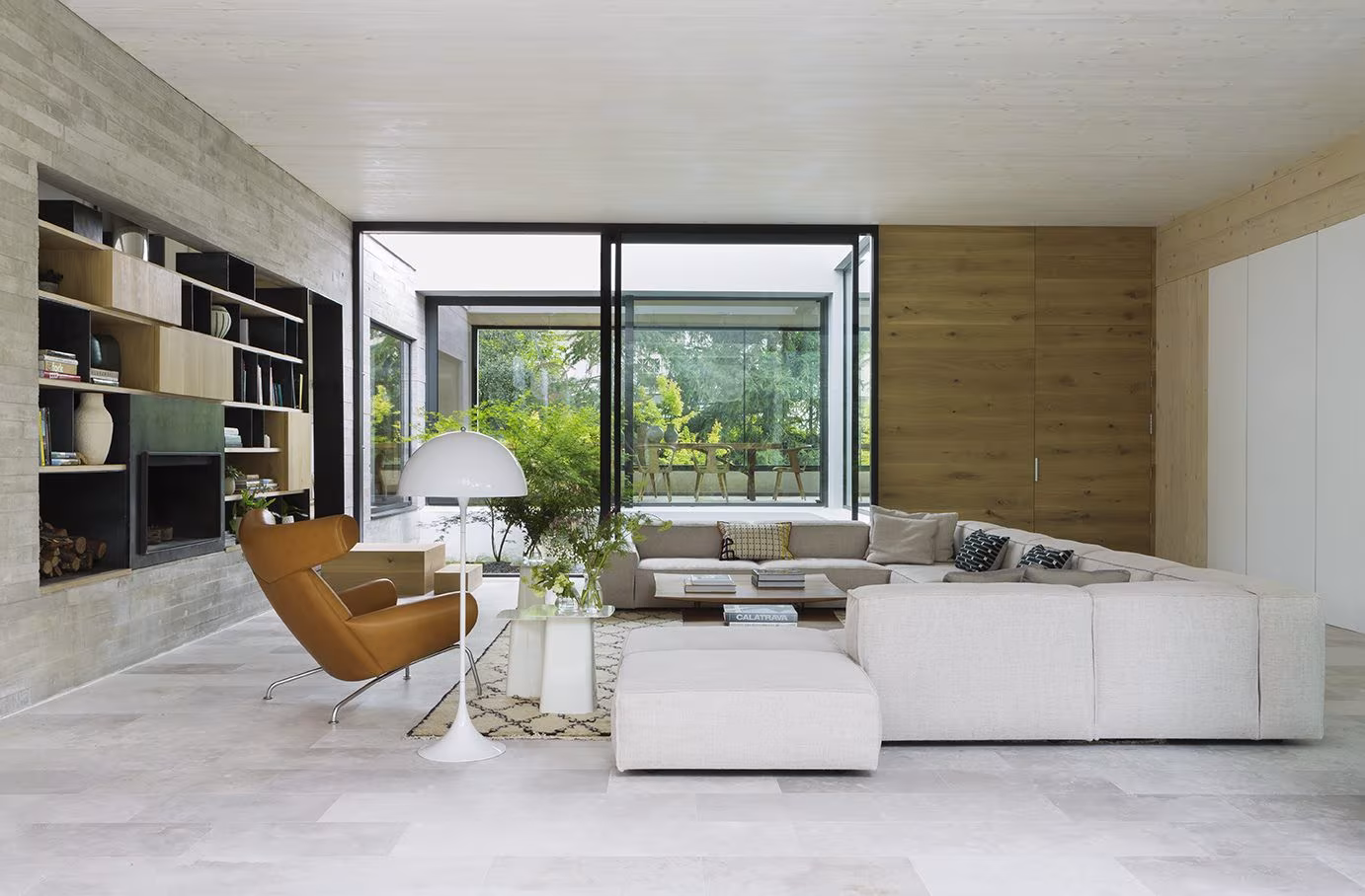 Salón de la casa CH con sofá modular blanco, librería y butaca naranja junto a un patio interior