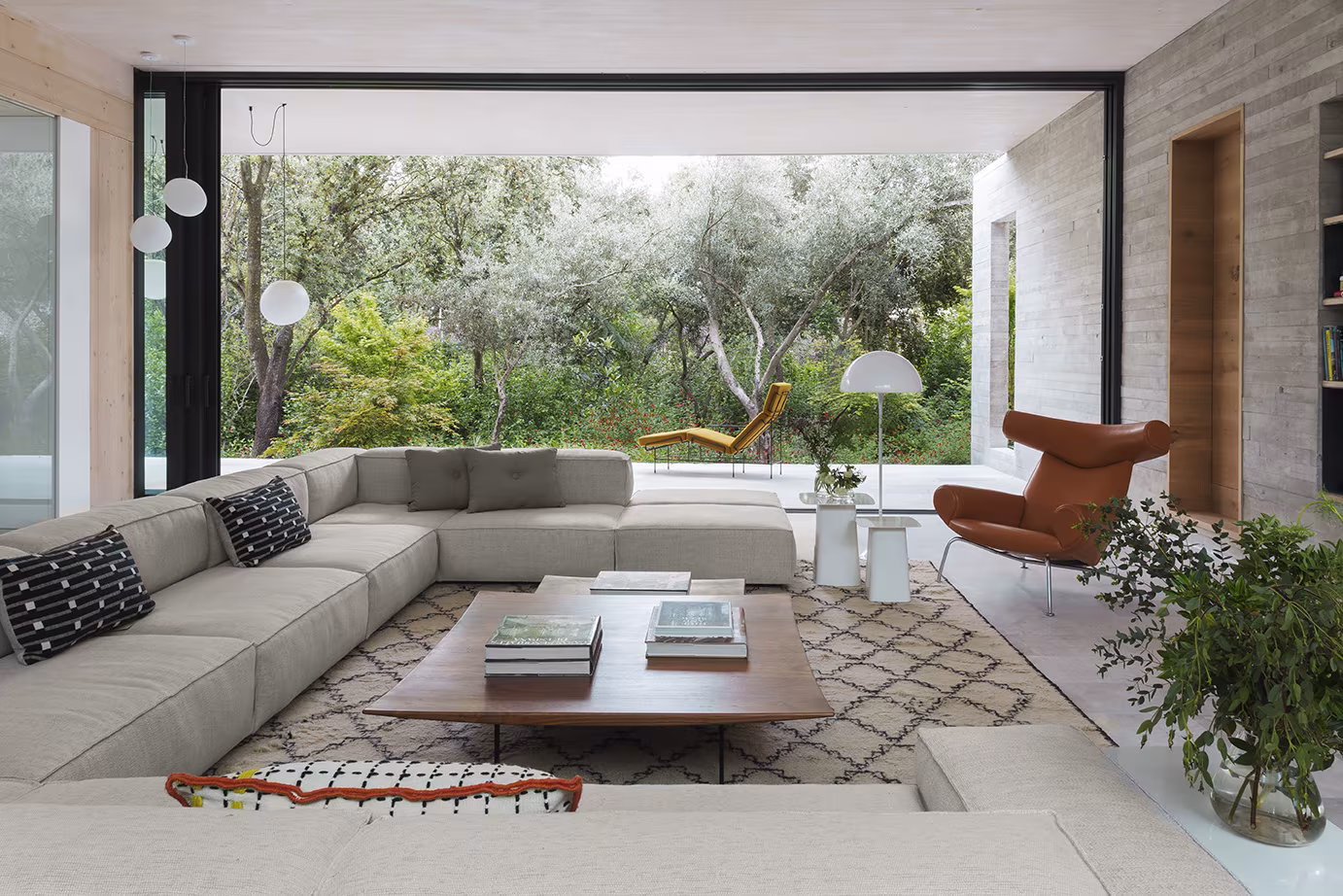 Salón hundido con sofá en L, mesa baja de madera y gran hueco al jardín de olivos en el Proyecto CH de ÁBATON