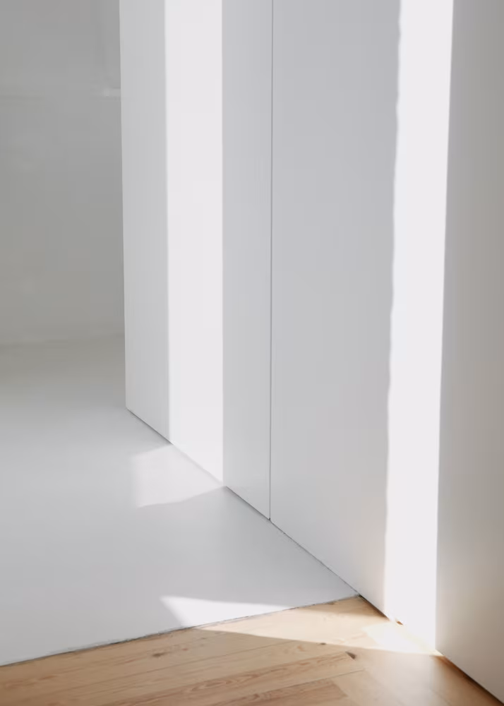 Rincón minimalista con paredes y suelo blancos, zona con tarima de madera clara, luz natural y estética limpia y serena.