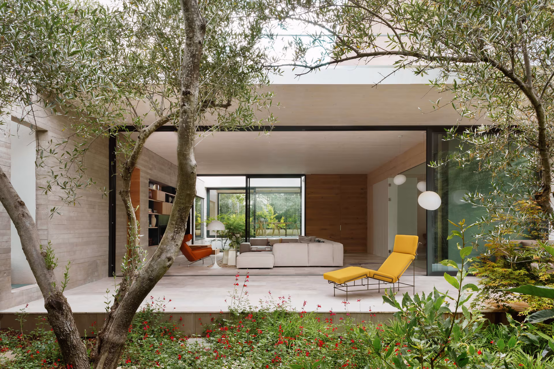Casa Brisa by Ábaton, a glazed living room opening onto a garden with olive trees and a yellow armchair