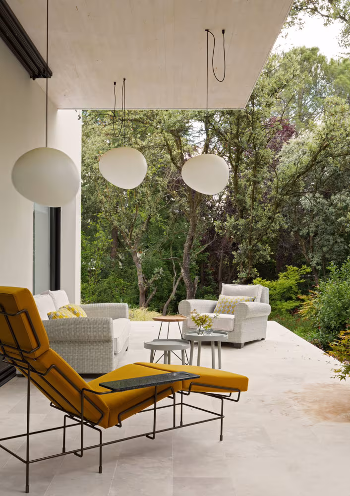 Terraza cubierta con chaise longue amarilla, butacas y lámparas esféricas ante el bosque en el Proyecto CH
