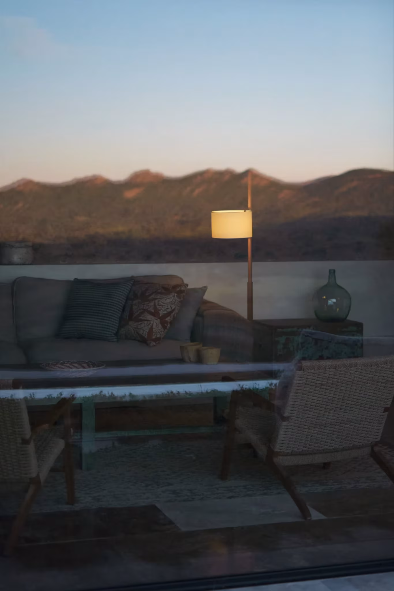 Salón al atardecer tras el cristal, con lámpara de pie encendida y montañas al fondo, en el artículo sobre Miguel Milá