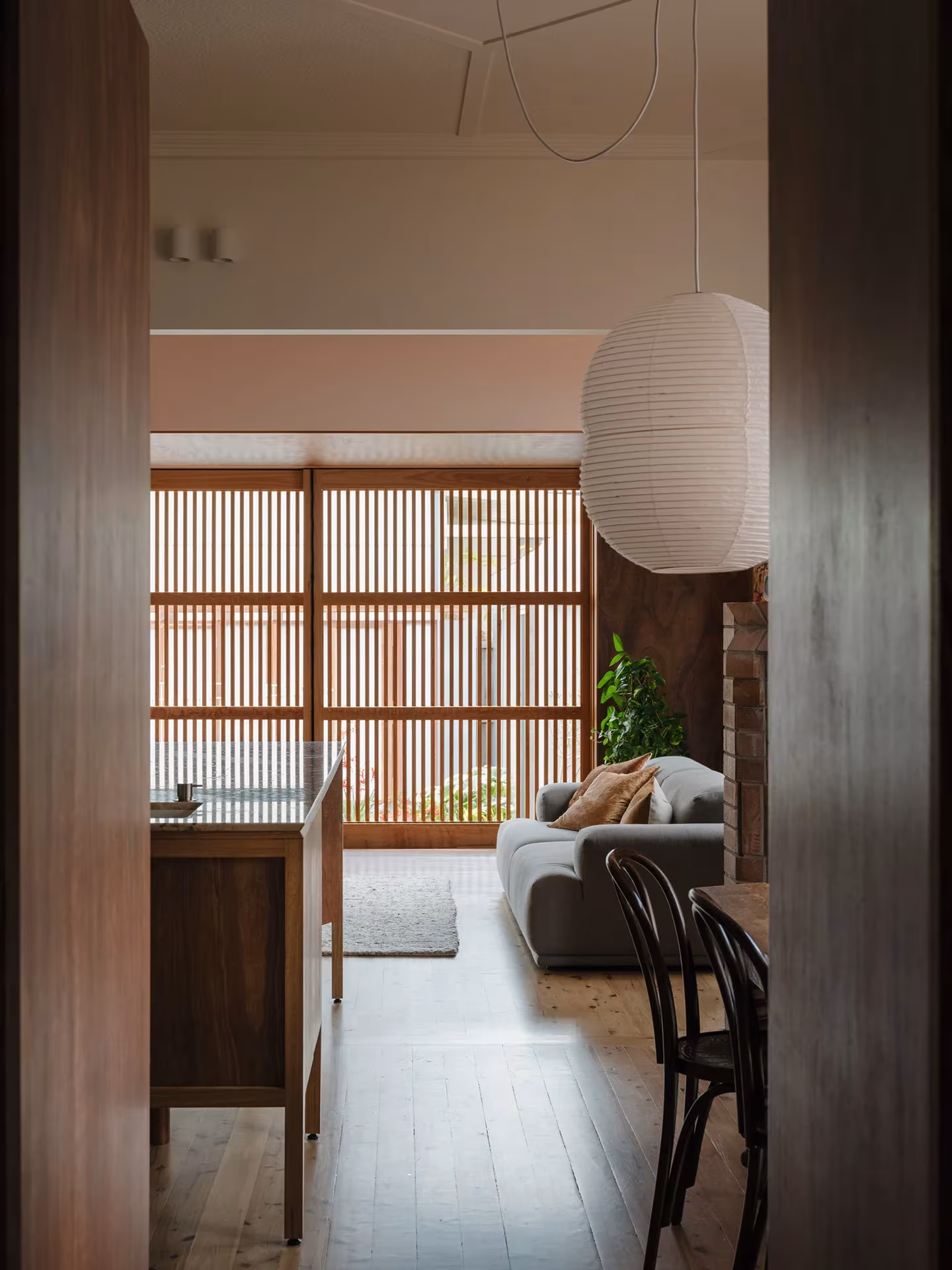 Vista desde la entrada de la Aru House hacia la cocina y el salón, con celosía de listones de madera al fondo
