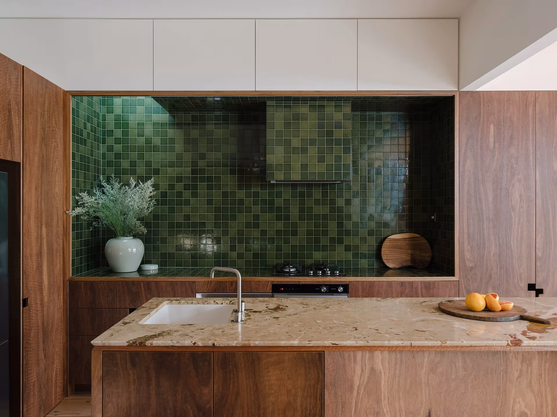 Cocina de la Aru House con revestimiento de azulejos verdes, mueble de madera e isla con encimera de piedra