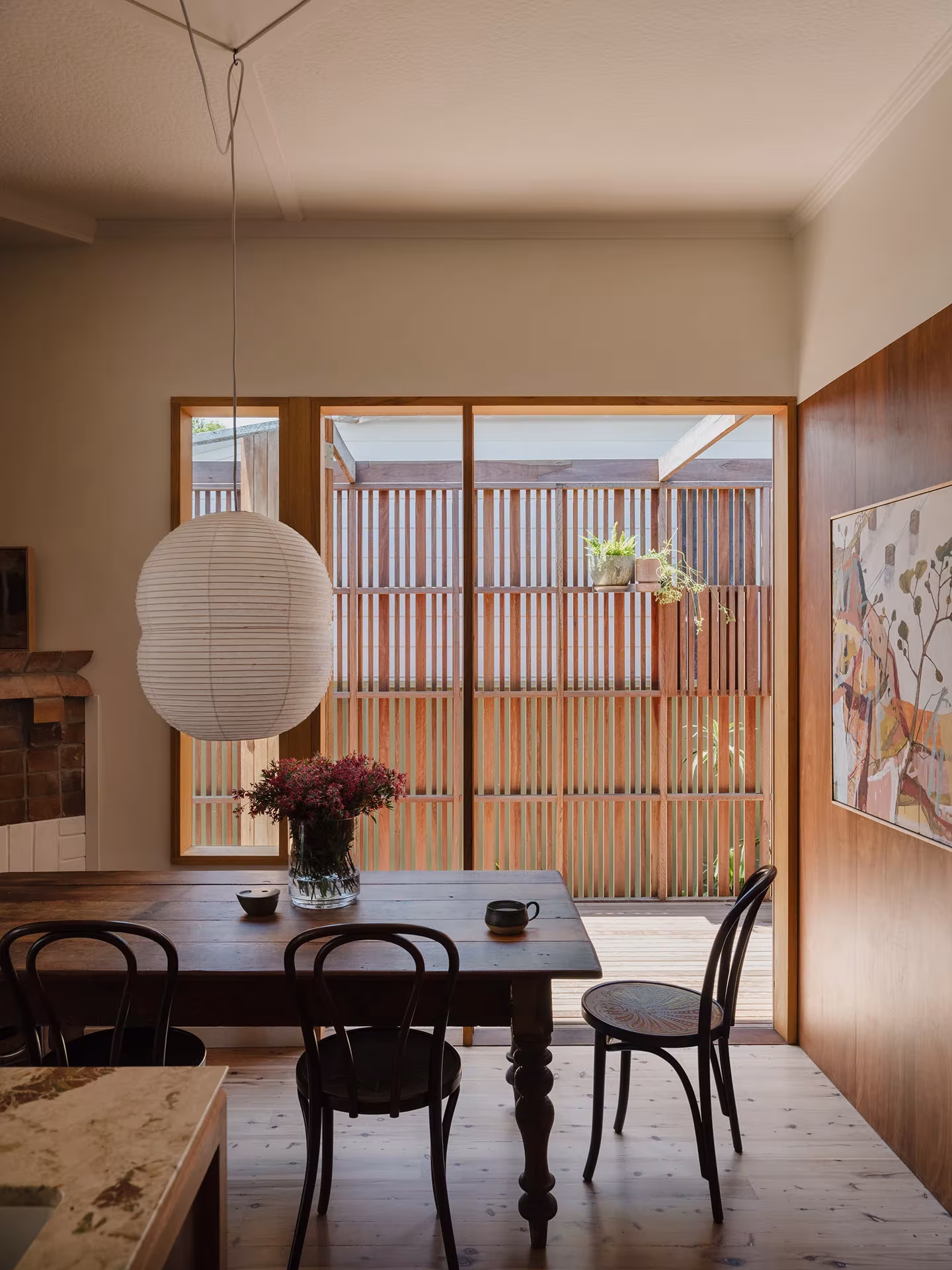 Comedor de la Aru House con mesa de madera, sillas de rejilla y gran ventana a un patio con celosía de listones