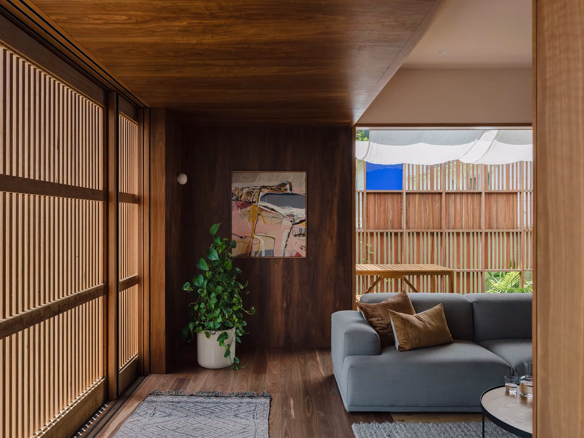 Sala de estar de la Aru House revestida de madera, con celosías correderas de listones abiertas al patio