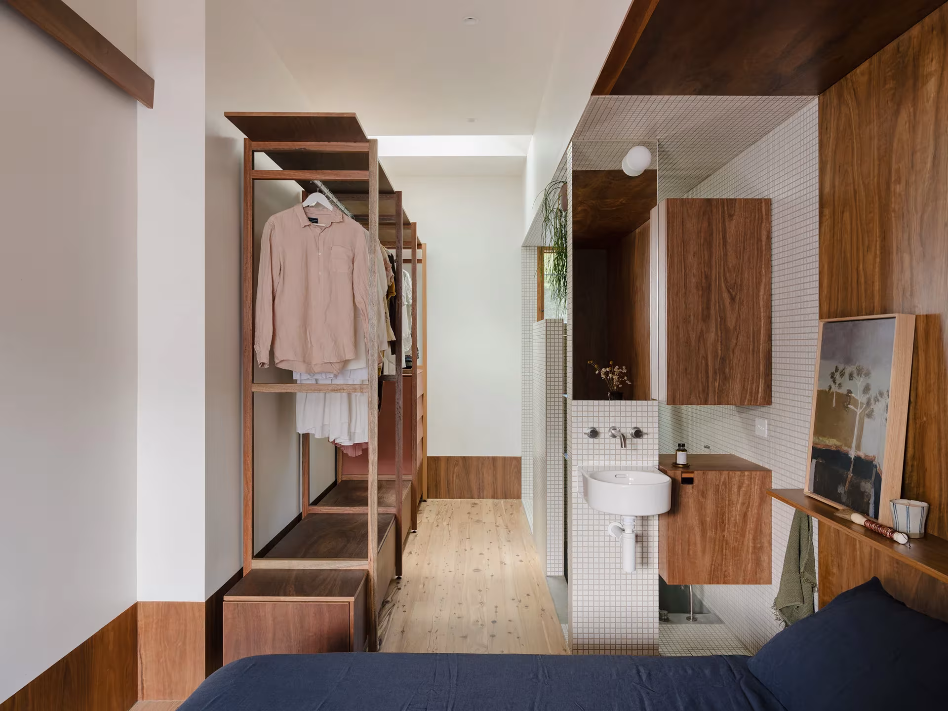 Dormitorio de la Aru House con armario abierto de madera, baño al fondo y suelo de tarima clara
