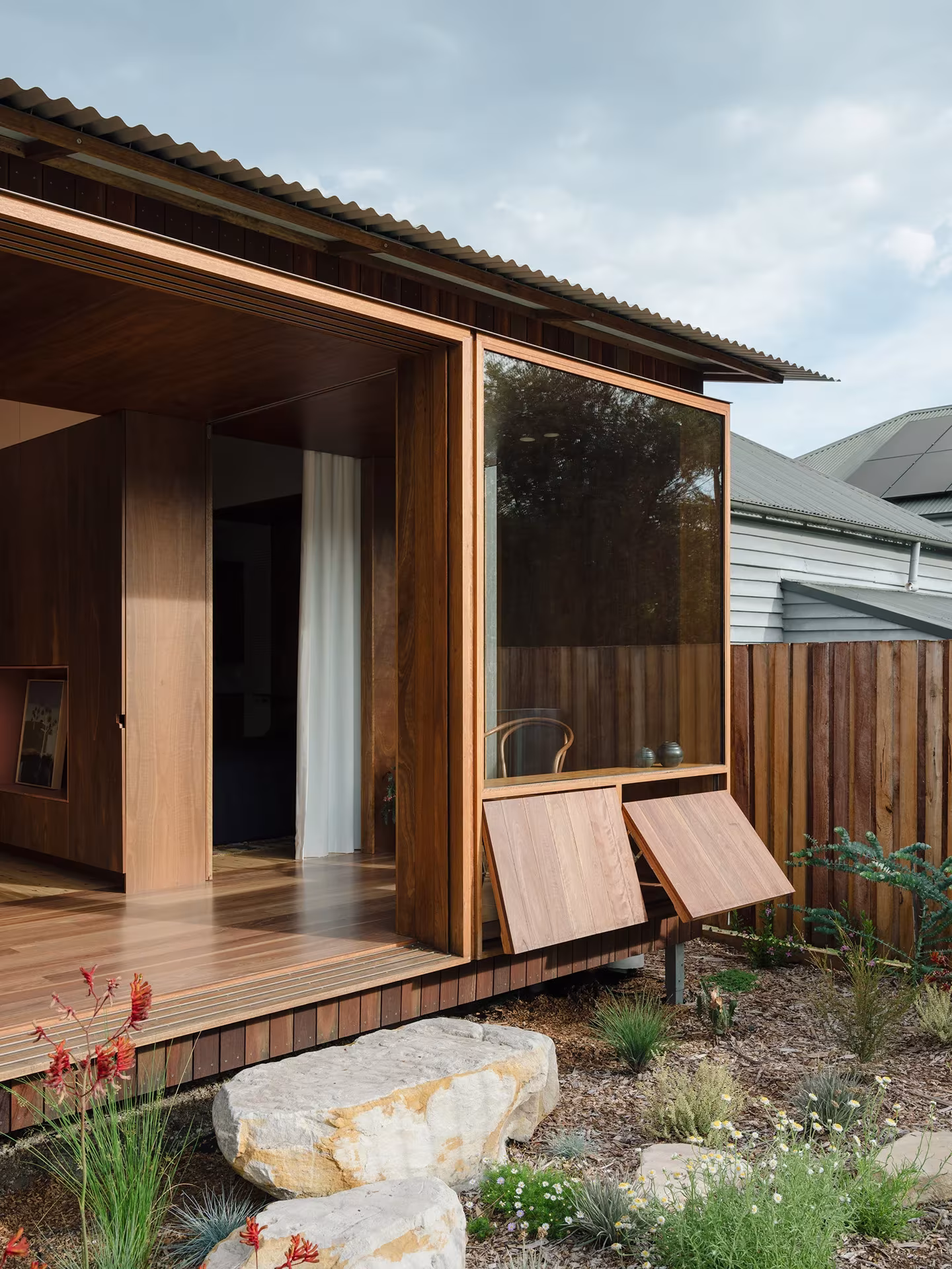 Volumen de madera de la Aru House con cubierta inclinada, gran ventana y contraventanas abatibles sobre el jardín
