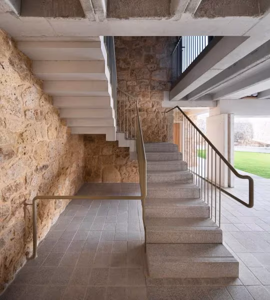 Escalera de hormigón con peldaños en voladizo junto a un muro de mampostería en la Casa Consistorial de Valverde de Campos