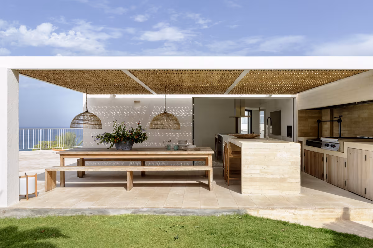 Cocina exterior mediterránea con techo de cañizo, encimeras de piedra beige y vistas al mar