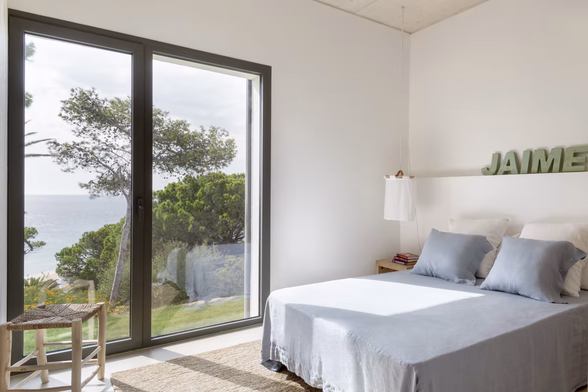 Dormitorio mediterráneo con vistas al mar, ropa de cama azul claro y lámpara colgante de tela